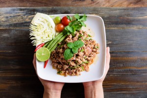 Thai Food, Spicy Minced Pork Salad (larb Moo) On White Dish Holding By Hand On Wooden Background, Top View