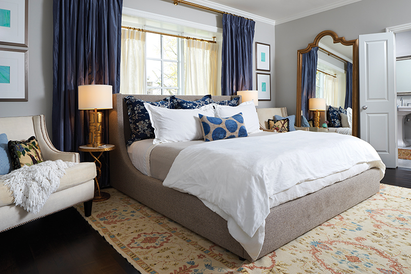 Here in the master bedroom we see elements borrowed from other rooms in the home, the repetition of which lends a sophisticated visual cohesion to the entire space. Club chairs from the living room are invited in, one in its original size and one that has been reimagined slightly as a settee. Window treatments mirror those in the master bath, and the burnished dark floor is topped with a traditional wool rug.