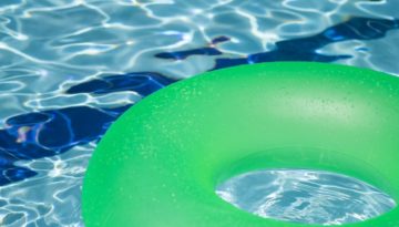 A bright green floating tube sits on light blue swimming pool water.