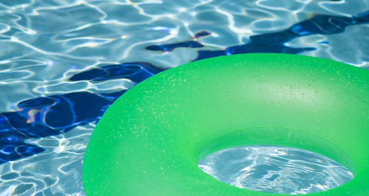 A bright green floating tube sits on light blue swimming pool water.