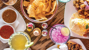 An assortment of chips, salsas, margaritas and other Tex-Mex dishes from El Huevo Mex-Diner lie on a wooden surface.
