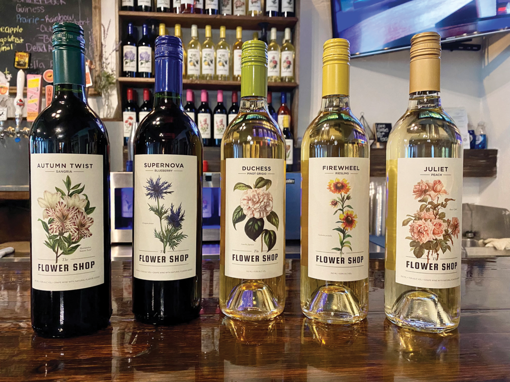 Five wines, two reds and three whites, from Flower Shop Winery are displayed on a bar table.