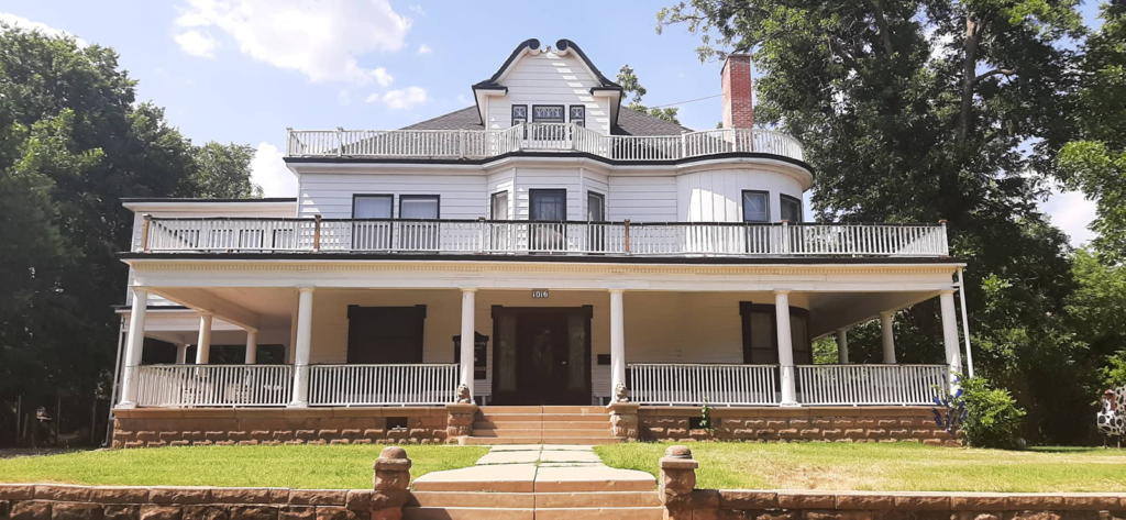 The Stone Lion Inn in Guthrie is brightly lit by daylight. Its grand patio wraps completely around the building and has a second-floor patio above it. The white house has a old-timely feel.