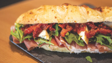 A sandwich from Ganache Patisserie with deli meats, spinach, peppers and other toppings on toasted sub bread.