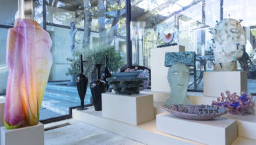 Pieces from the Rose Family Studio Glass collection are placed on cubed display stands in a home. The pieces range from refined black functional-resembling pottery to opaque busts of heads.