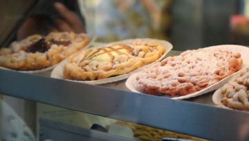 Three flavors of funnel cake sit in a display at a food vendor at a state fair.