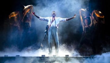 Chibueze Ihuoma exclaims on a foggy stage wearing a guitar on his back during a touring production of Hadestown.