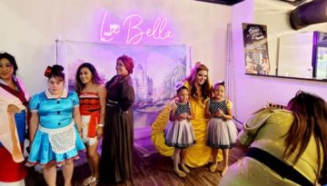 Young models pose for photos with experienced one in front of a backdrop illuminated with a neon sign reading "La Bella."