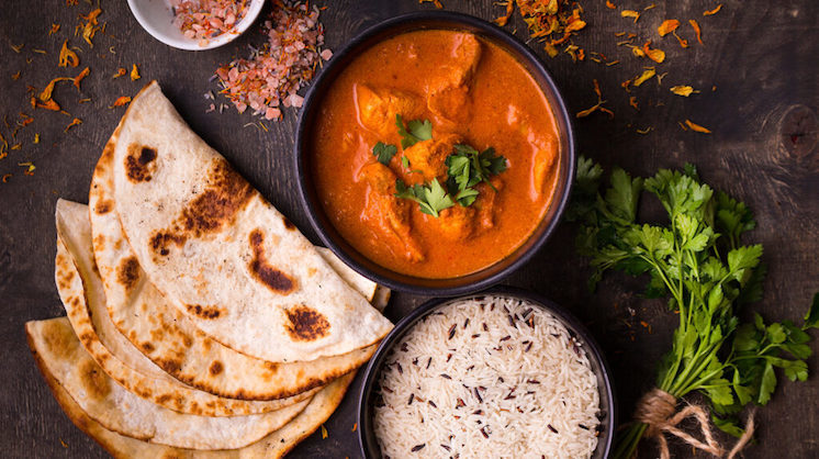 A table of basmati rice, naan and an orange curry chicken are viewed from the top of a table.