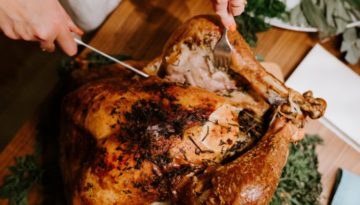 A person cuts through a fully cooked turkey with a large knife.