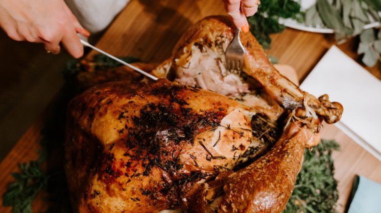 A person cuts through a fully cooked turkey with a large knife.