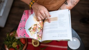 A person holds open a cookbook and runs through the recipe with their finger.