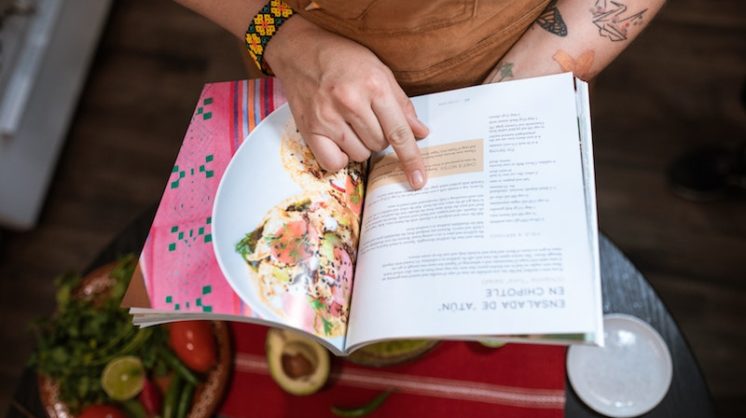 A person holds open a cookbook and runs through the recipe with their finger.