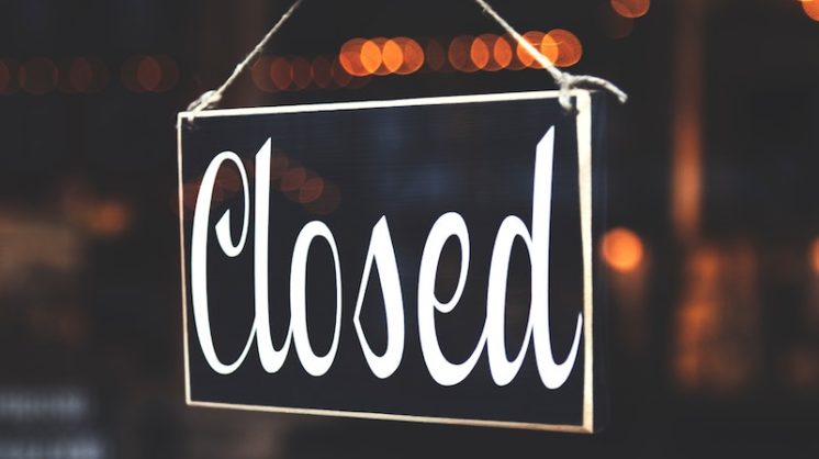 A sign hanging on a glass door reads "Closed."