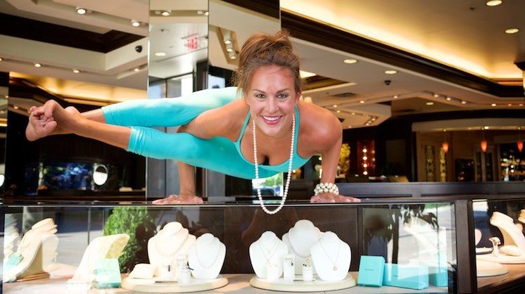Yoga instructor and Flo State founder Tiffany Porte Woodruff holds a horizontal pose by her two arms where both legs point straight to her right. She's on top of a jewelry display case.
