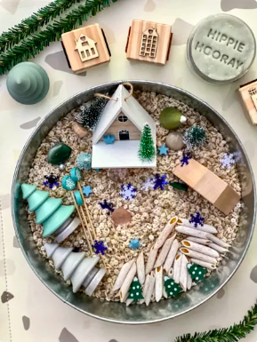 A sensory kit that features a small cabin, trees, stars and pastas in a pile of star-shaped pasta.