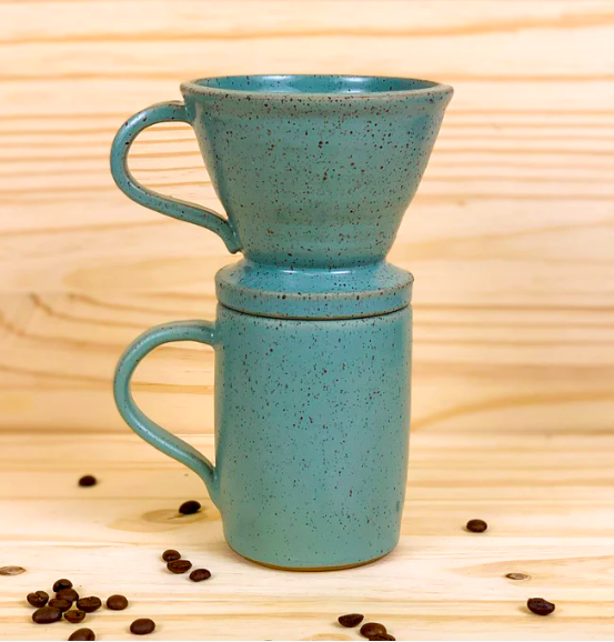 A smooth turquoise ceramic coffee mug with the same color pour-over filter on top of it.