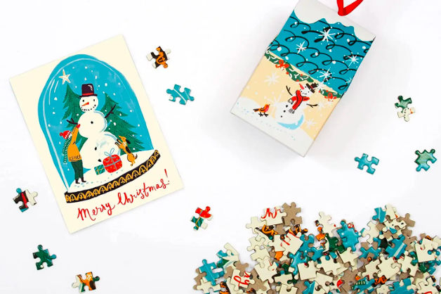 A box ornament that holds puzzle pieces that make up the image of a snow globe.