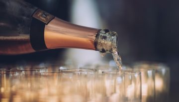 A bottle of sparkling wine pours in a spread of many different glasses.