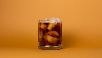 A glass of iced cold brew coffee sit on an orange background.