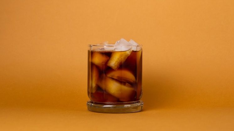 A glass of iced cold brew coffee sit on an orange background.