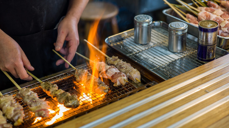 A chef cooks yakitori over a flame grill.