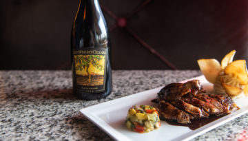 A dish of cooked meat and vegetables served in a cylinder shape sits next to a bottle of red wine.
