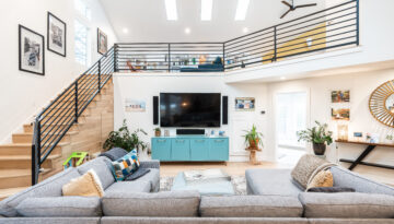 A bright living room with a sectional sofa and blue TV stand has an overview with three windows pouring in light at the Quail Creek Home Tour.