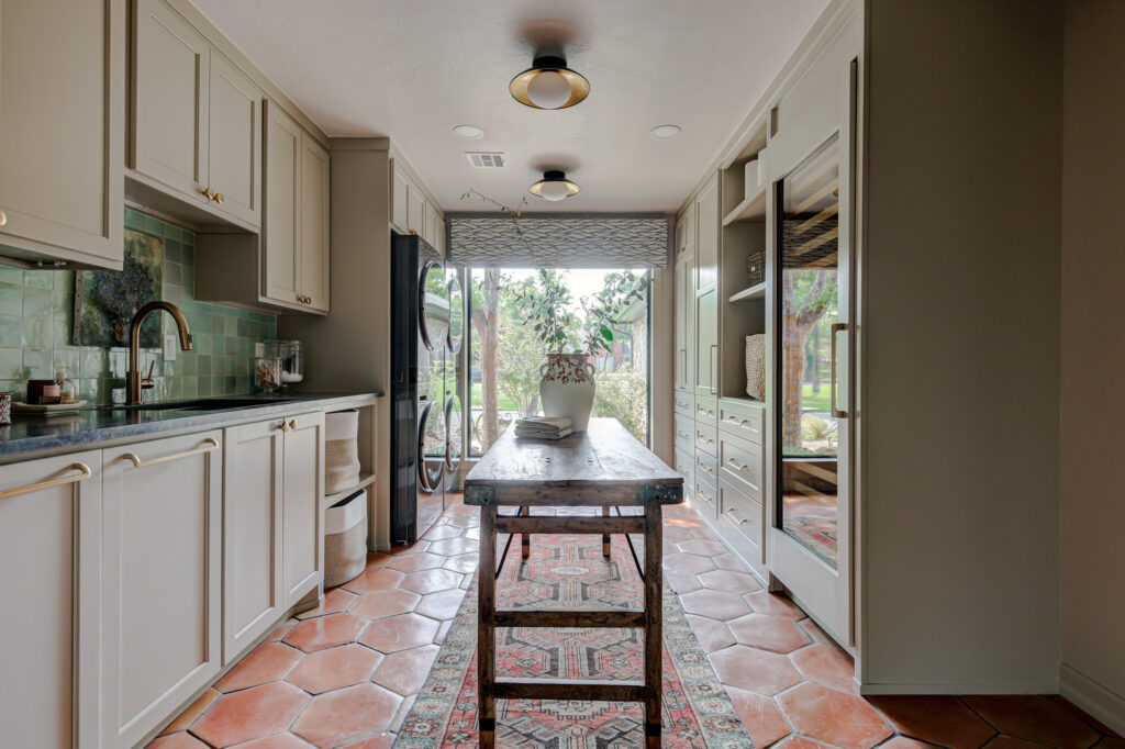 Large laundry room in an Edmond home featuring Saltillo tile floors, green tile backsplash and long, rustic table