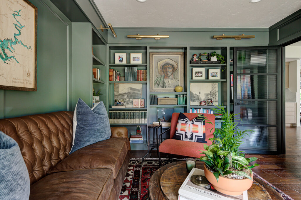 A study in an Edmond home featuring a green wall with paintings, leather couch, and greenery