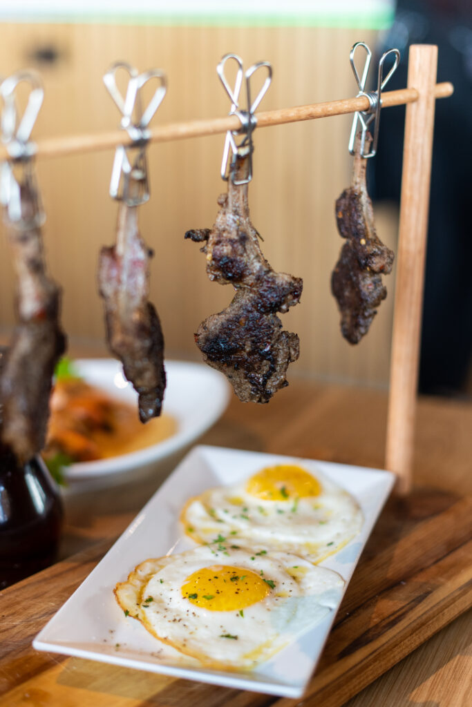 Four seared lamb chops hanging above two over easy eggs at Scrambld