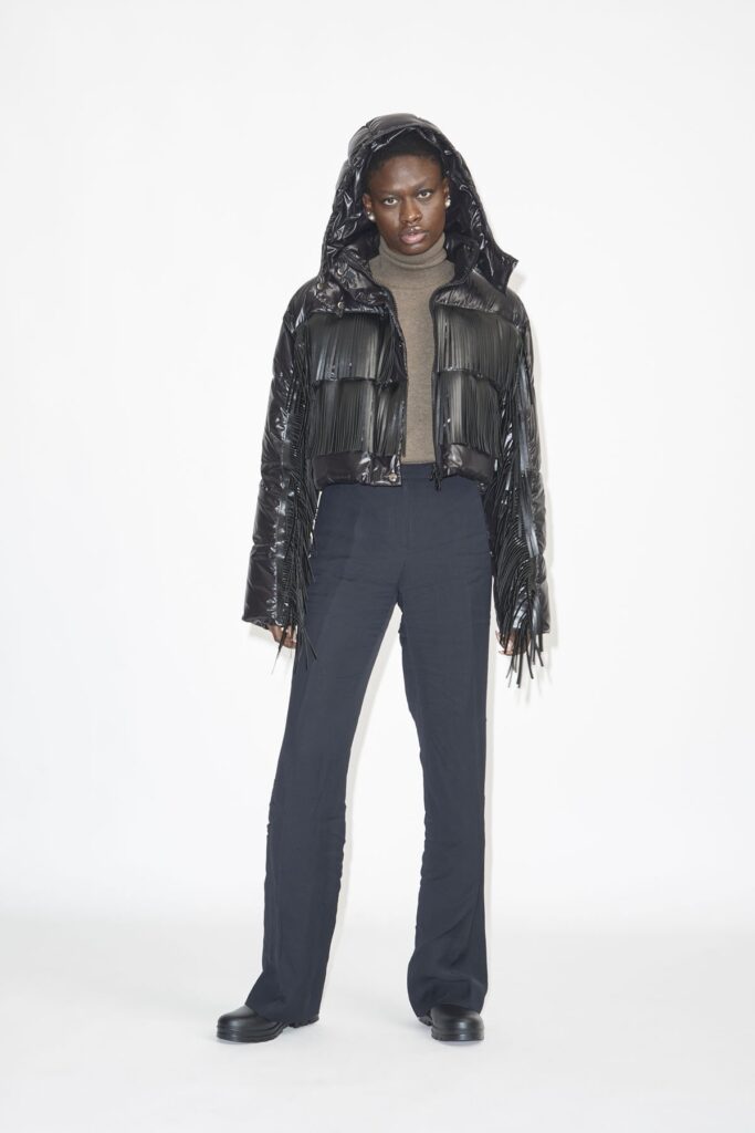 Woman wearing a tan sweater with a black puffer jackets with fringe