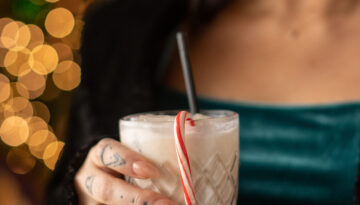 Woman in green shirt holding a white cocktail with a candy cane