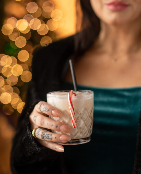 Woman in green shirt holding a white cocktail with a candy cane