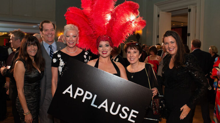 five people posing with a showgirl, who has on a headpiece of large red feathers