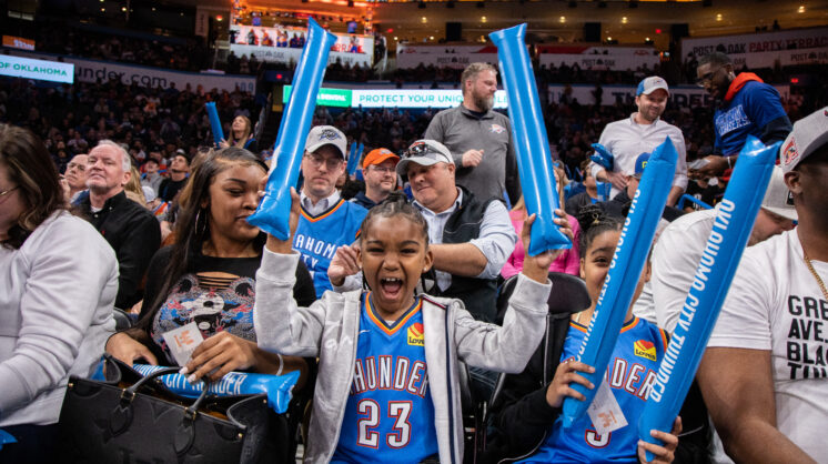 Young OKC Thunder basketball fan at game cheering with blue balloons