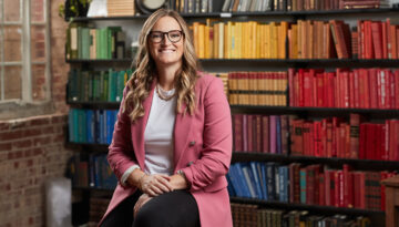 Author Allison Ashley poses in front of color coded bookcase