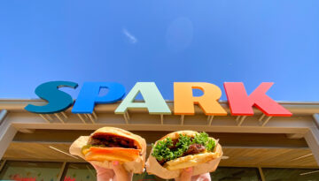 two burgers from Spark restaurant in OKC in front of a colorful sign from the restaurant