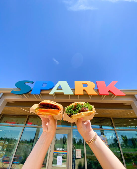 two burgers from Spark restaurant in OKC in front of a colorful sign from the restaurant