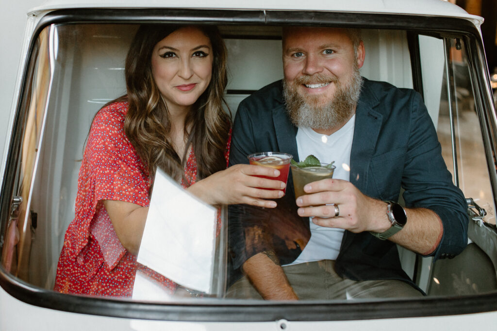 A man and a woman pose with drinks in a car
