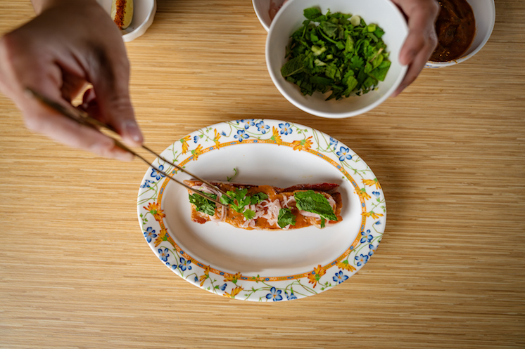 An elegant dish from Ma Der Lao Kitchen is being plated with a pair of small tweezers.